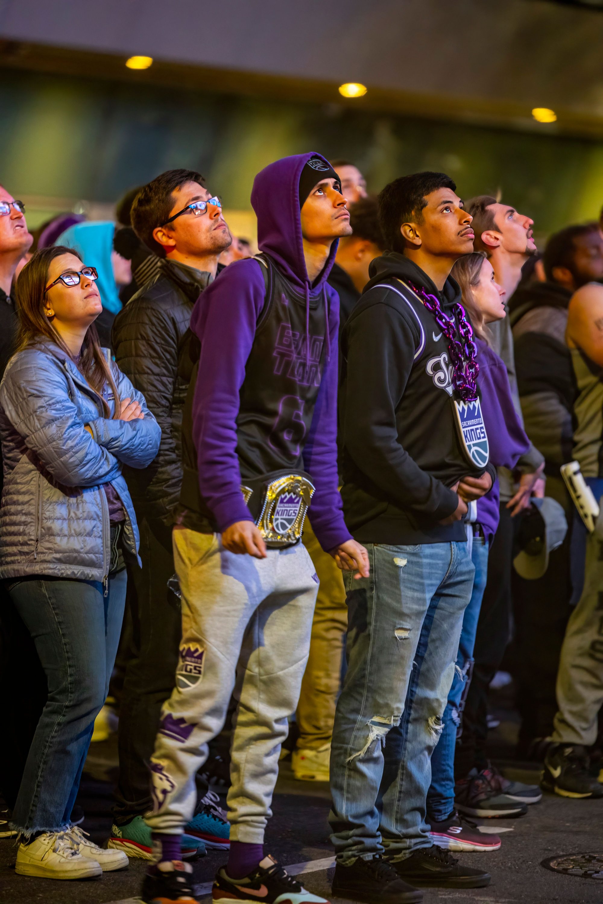A crowd of people standing close together, all attention drawn upward toward something outside the frame.
